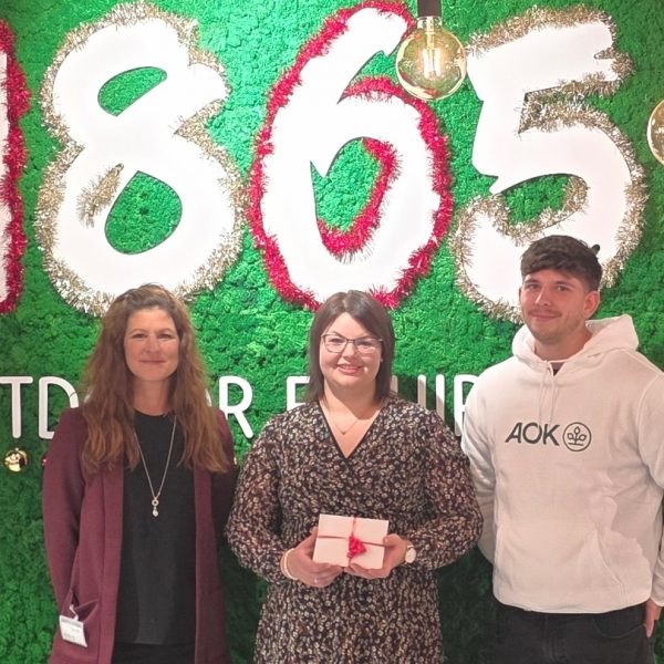 Das Foto zeigt die Gewinnübergabe durch Melanie Palta von 1865 Outdoor Equipment (links) und Marcel Hirner von der AOK Bayern (rechts) an die glückliche Gewinnerin Daniela Jehle (Mitte). Foto: AOK, Marcel Hirner