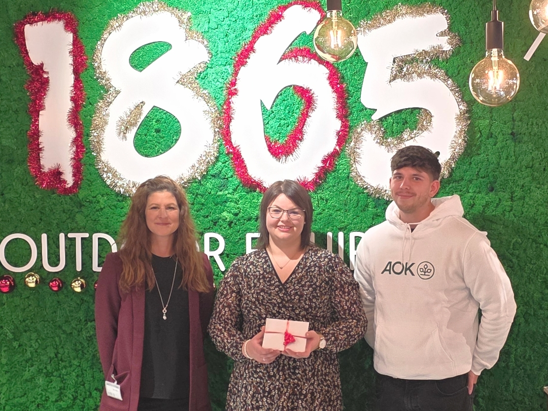 Das Foto zeigt die Gewinnübergabe durch Melanie Palta von 1865 Outdoor Equipment (links) und Marcel Hirner von der AOK Bayern (rechts) an die glückliche Gewinnerin Daniela Jehle (Mitte). Foto: AOK, Marcel Hirner